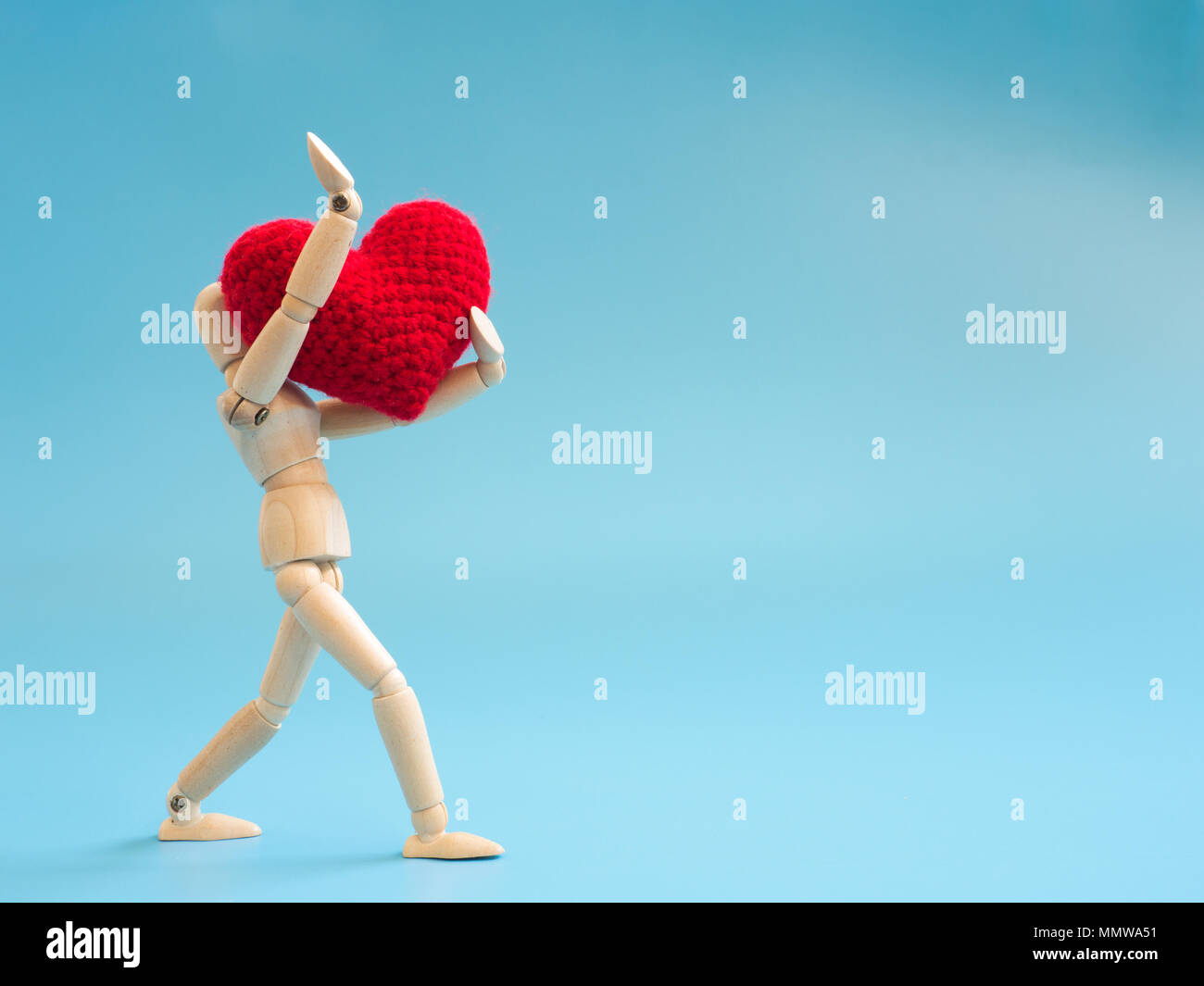 Wooden puppet walking and hold red heart on the sky blue screen