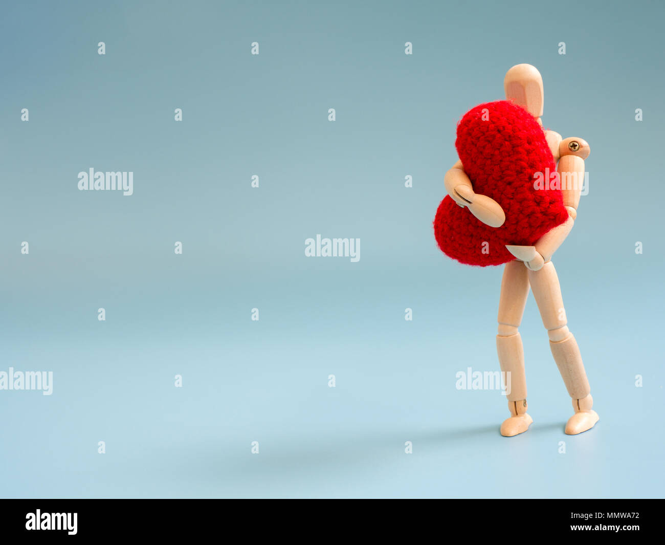 Wooden puppet standing and hold red heart on the sky blue screen