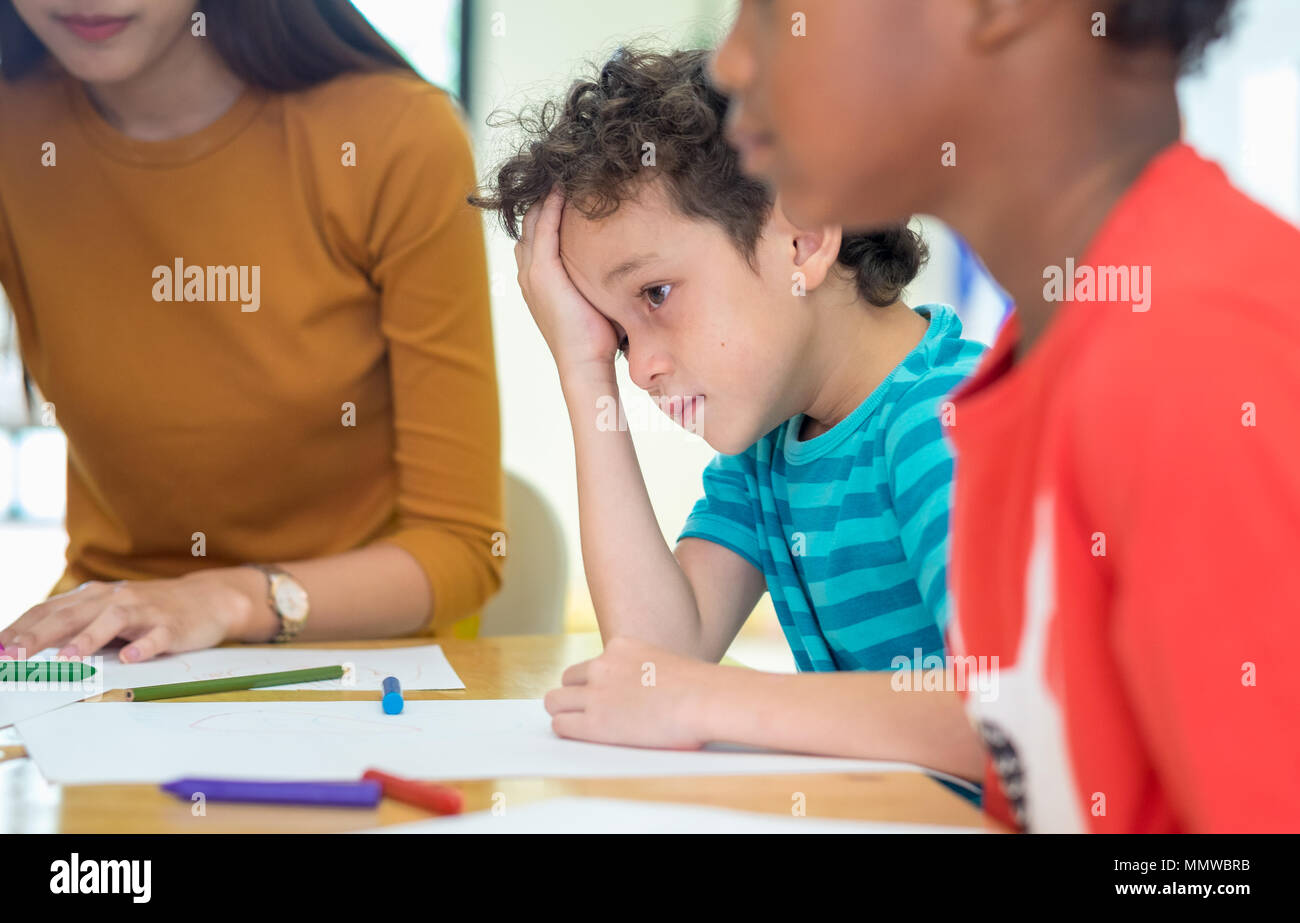Caucasion boy kid with sadness emotion sitting in classroom in kindergarten preschool.bulying depression concept Stock Photo