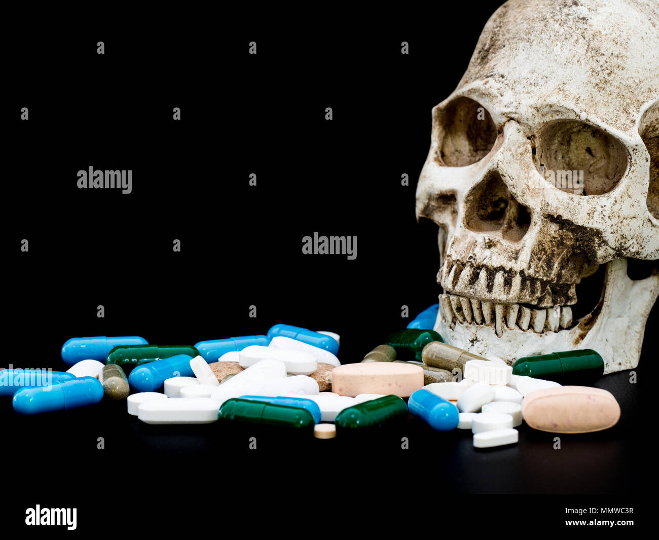 Human skull on multicolored of drug and capsule is on the black background. Close up. We are against drugs (anti drugs), cure in container for health. Stock Photo