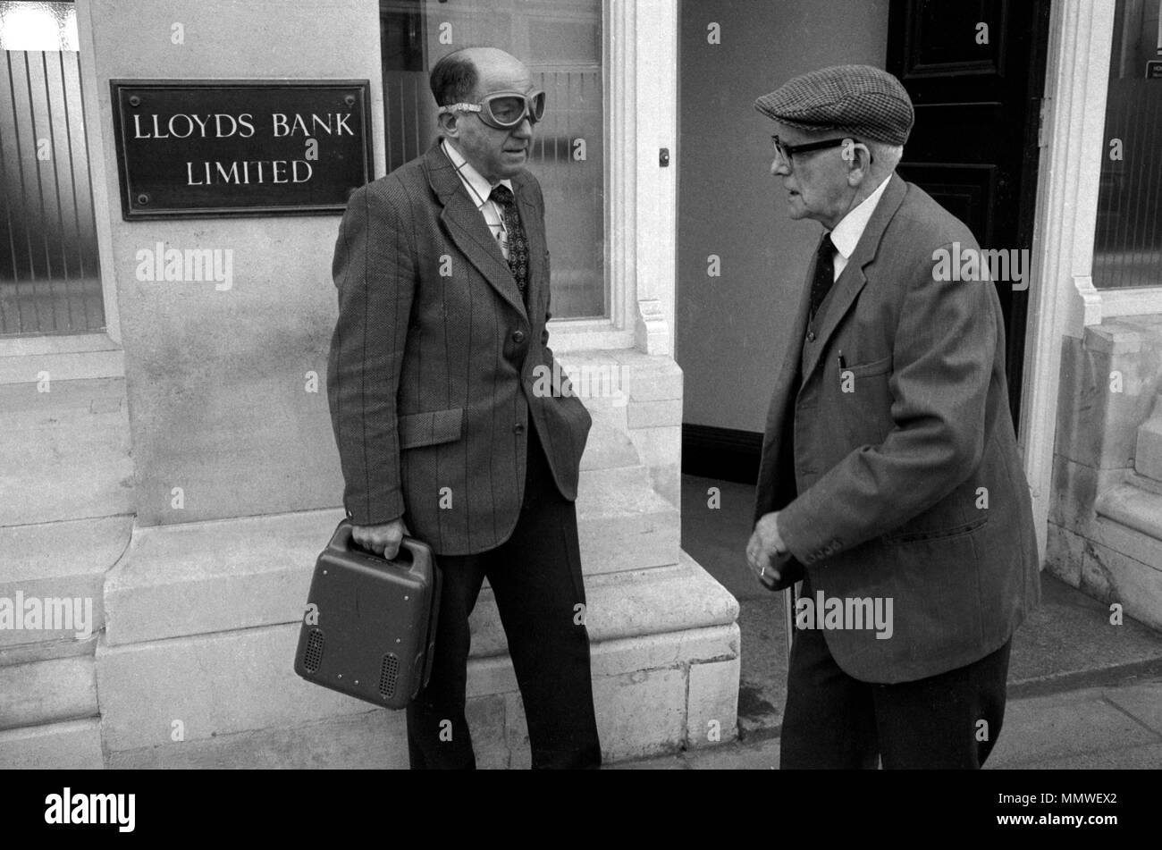 Bank courier delivering money etc 1970s UK. A middle aged balding security man delivering money in cash box to high street bank and wearing protective clothing, just  goggles 1979 70s HOMER SYKES Stock Photo