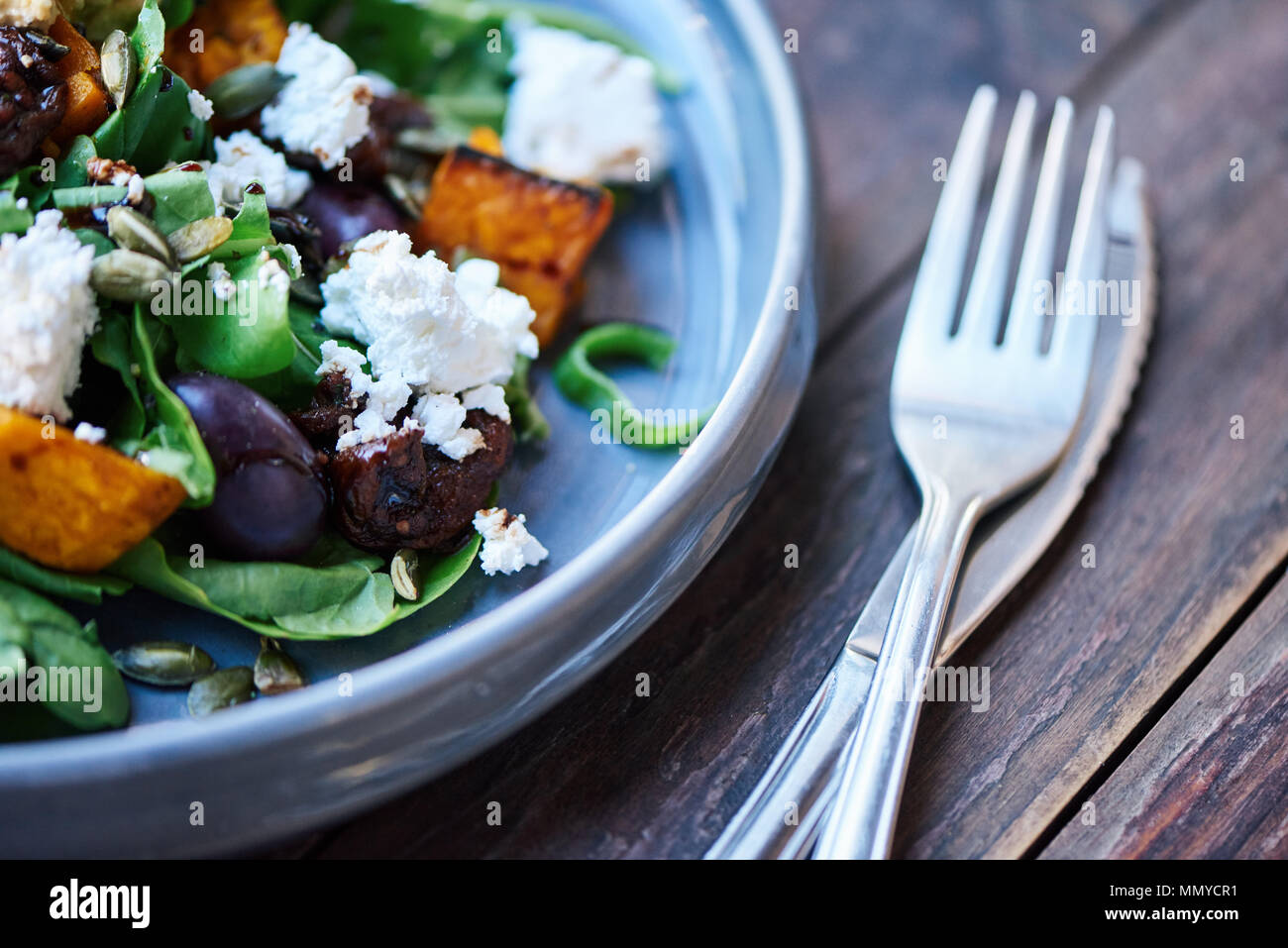 Delicious mixed salad sitting with cutlery on a wooden table Stock Photo