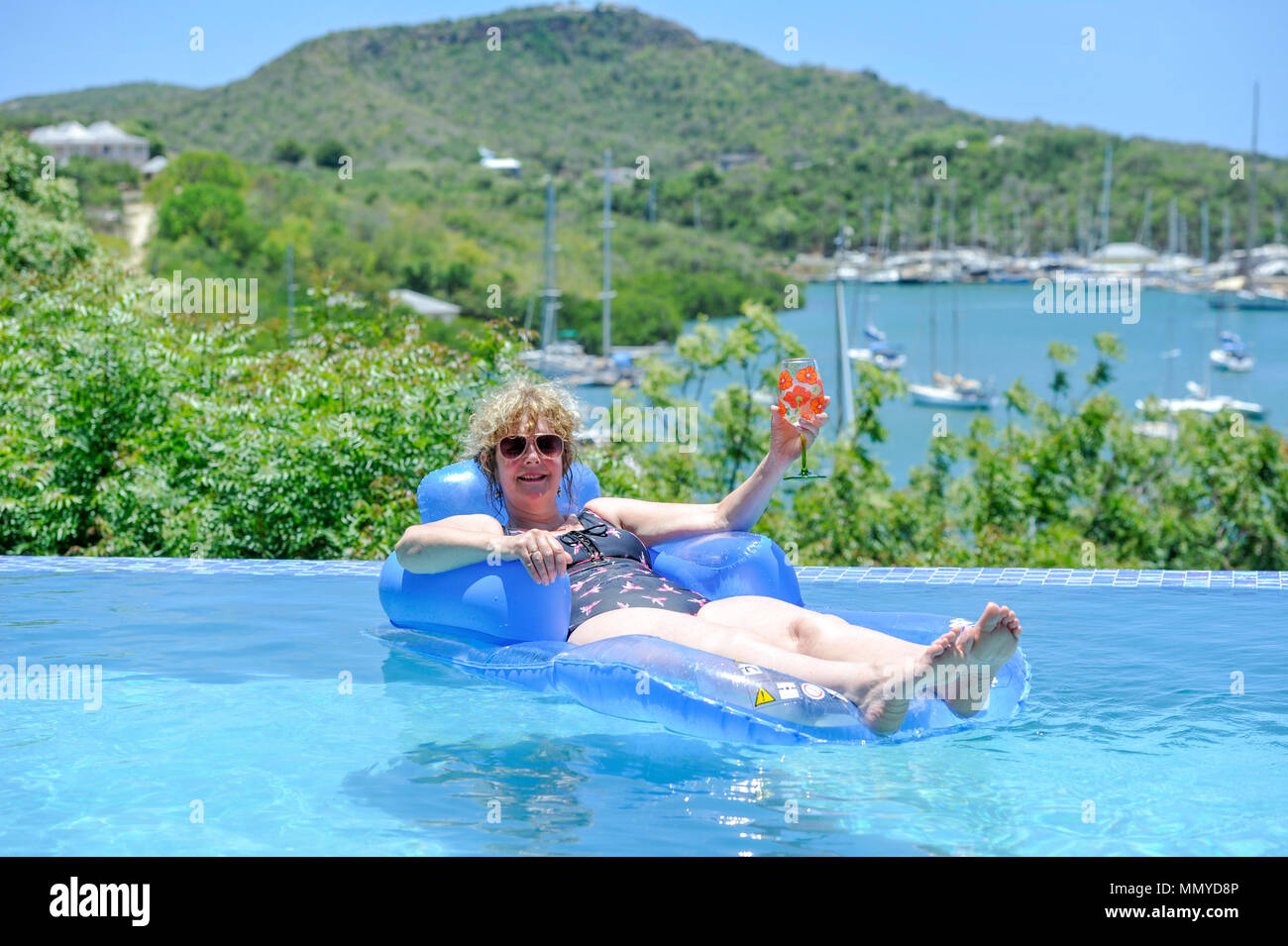 Antigua Lesser Antilles islands in the Caribbean West Indies - Woman on inflatable in an infinity swimming pool view overlooking English Harbour Stock Photo