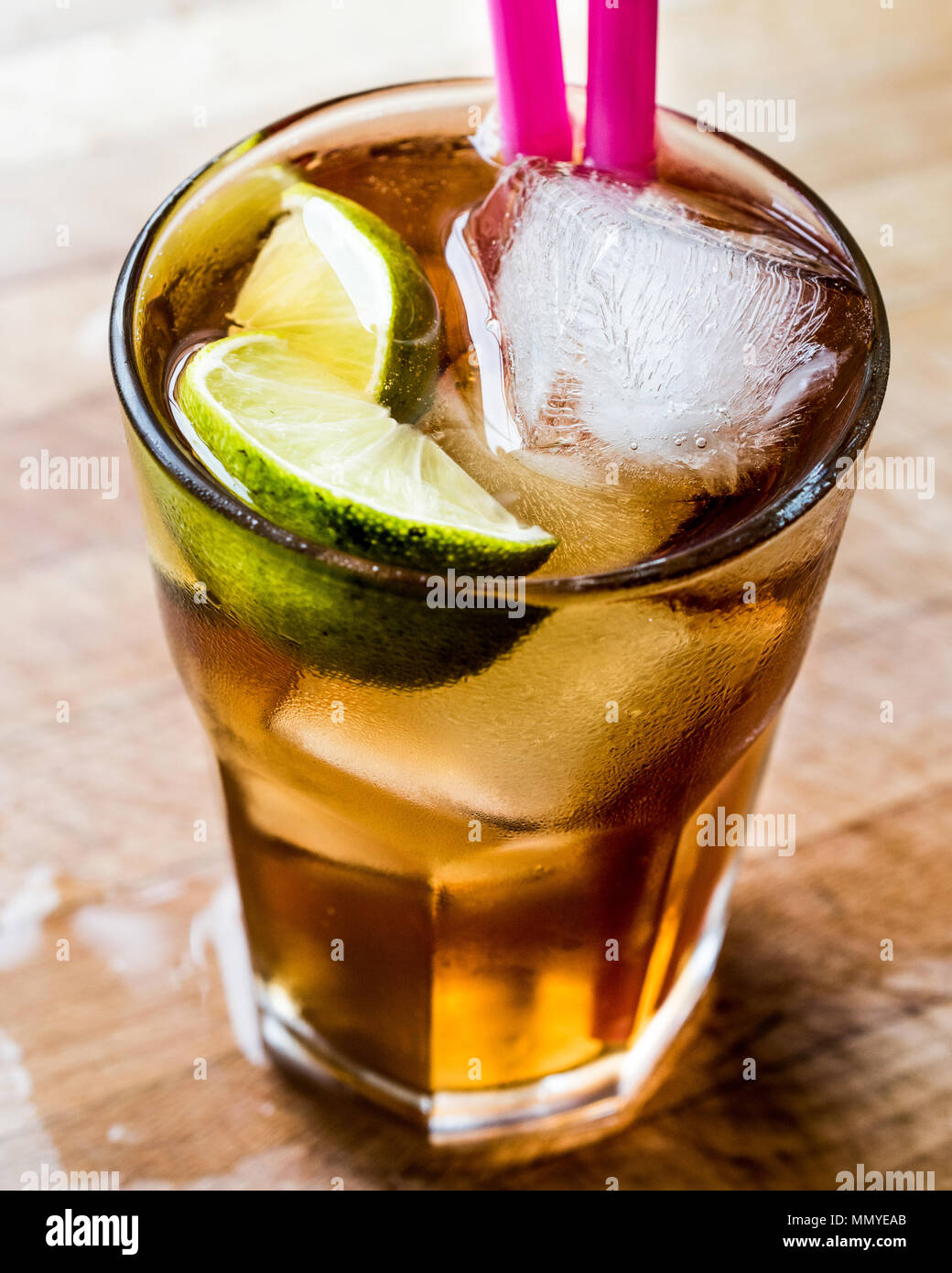 Long island iced tea cocktail with lime, ice and served with pink straw