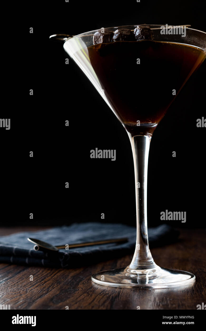 Black Manhattan Cocktail with olives on dark wooden surface. Dark