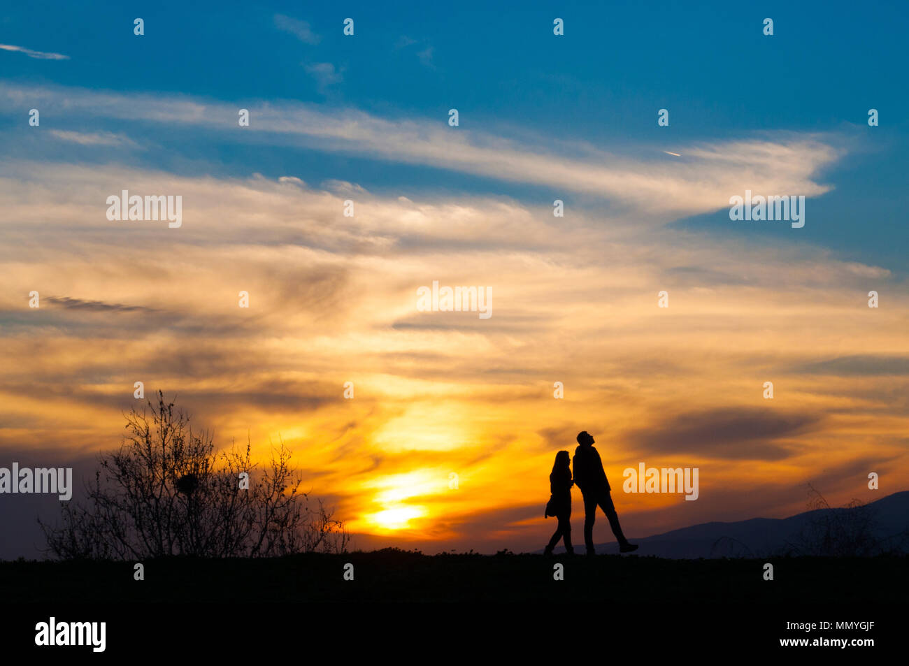 Love couple walking on sunset. Beautiful warm sky behind them Stock Photo