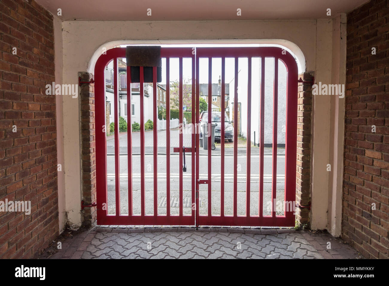 A red metal gate is locked at the exit to a car park. Stock Photo