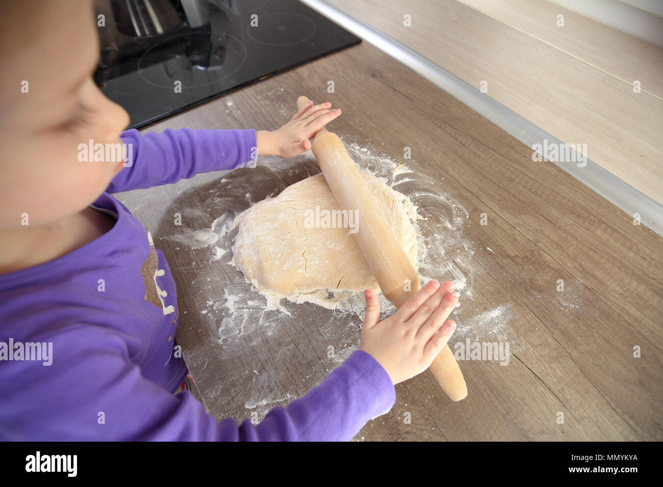 Little girl trying to cook. Baby girl with roller pin making gough. Stock Photo