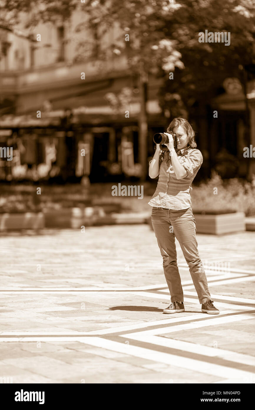 DIMITROVGRAD, BULGARIA - APRIL 30, 2018: Beautiful female photographer takes photos with her big black DSLR camera under the sun at street concert eve Stock Photo