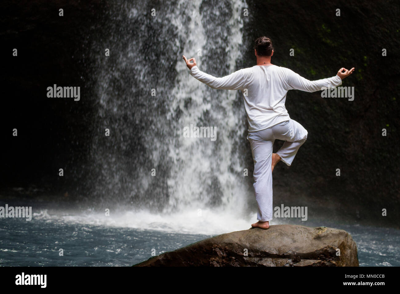 Man standing in meditation yoga on rock at waterfall Stock Photo
