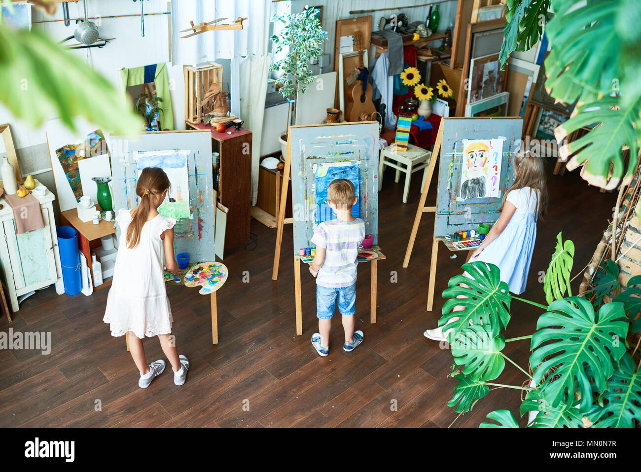 High angle portrait of three children painting on easels during art ...