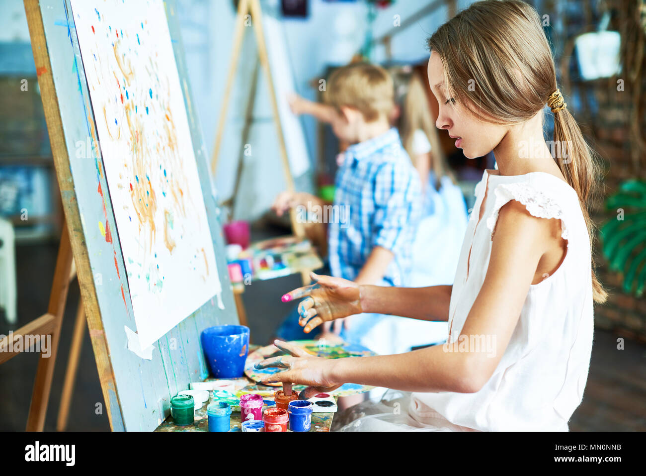 Side view portrait of talented teenage girl painting beautiful picture on  easel in art class, working with other children Stock Photo - Alamy
