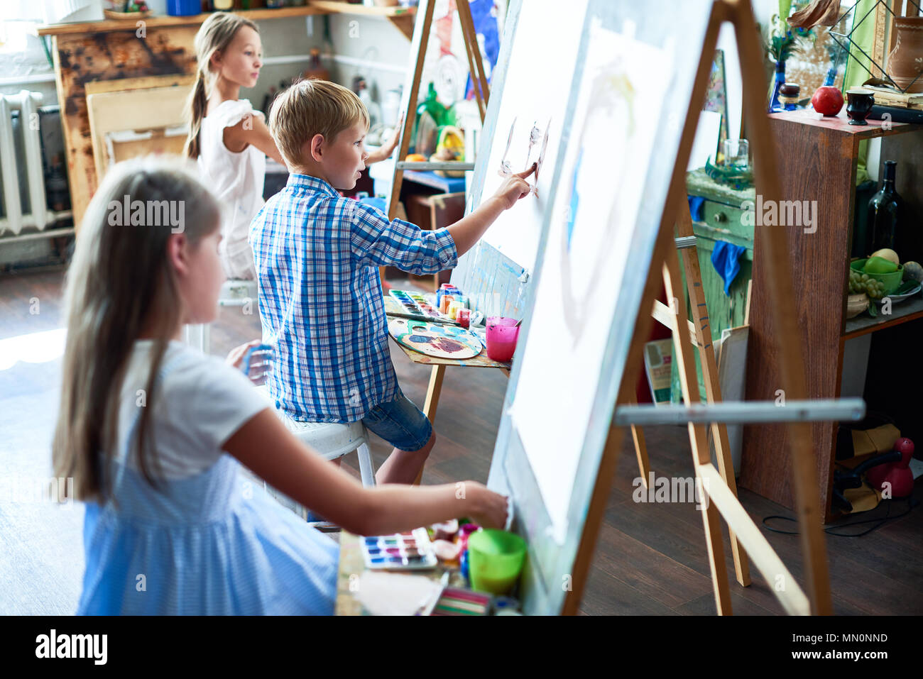 Side view portrait of three children painting on easels during art ...