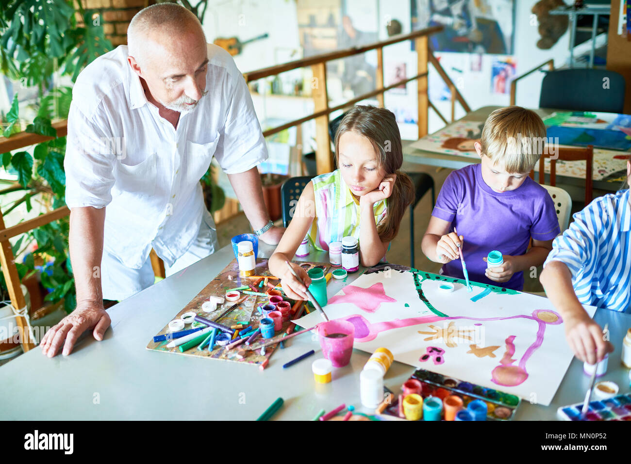 Portrait of three children painting pictures at table in art class with ...