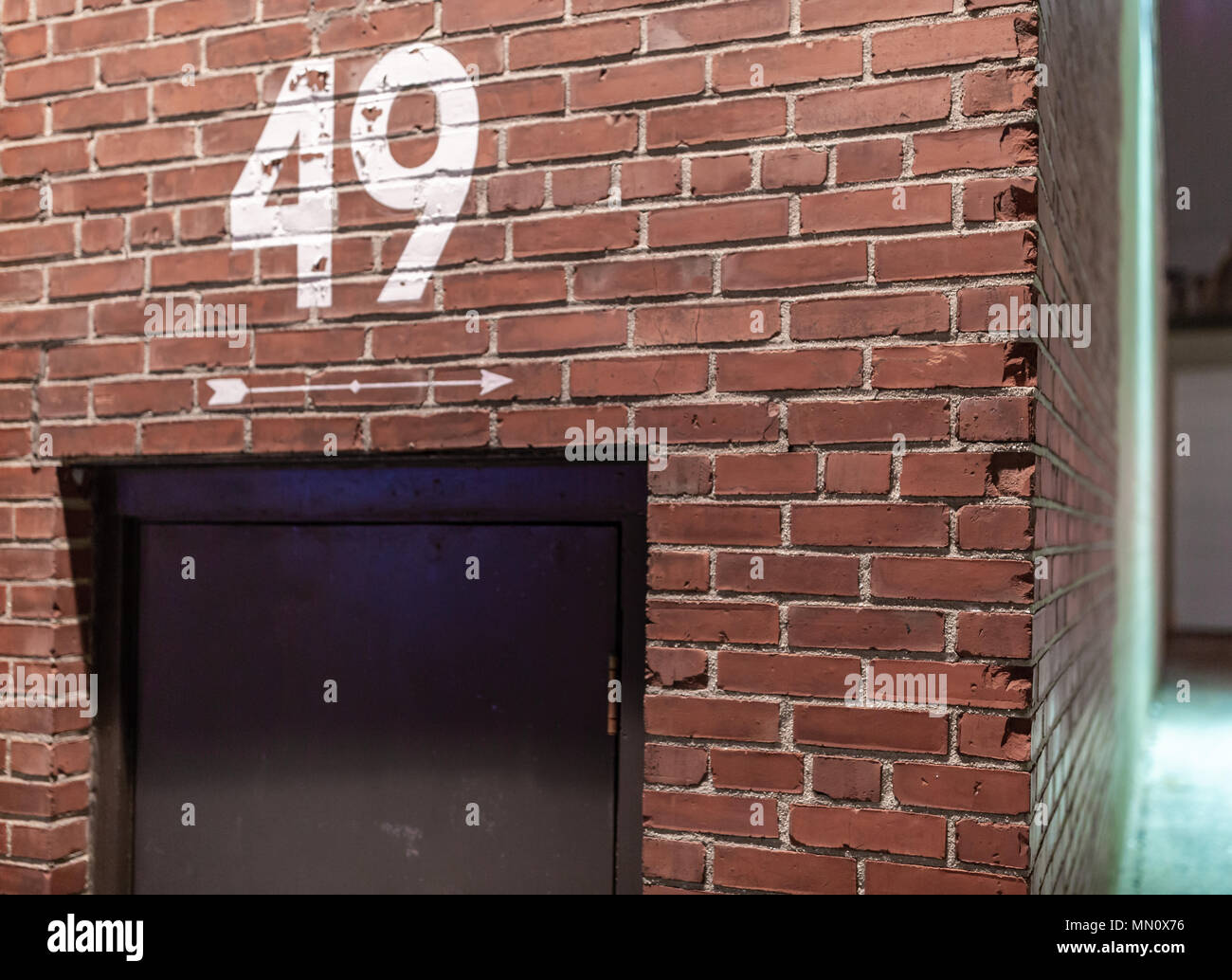 number 49 painted on a brick wall with a painted white arrow point down the side of the industrial building above a black door Stock Photo