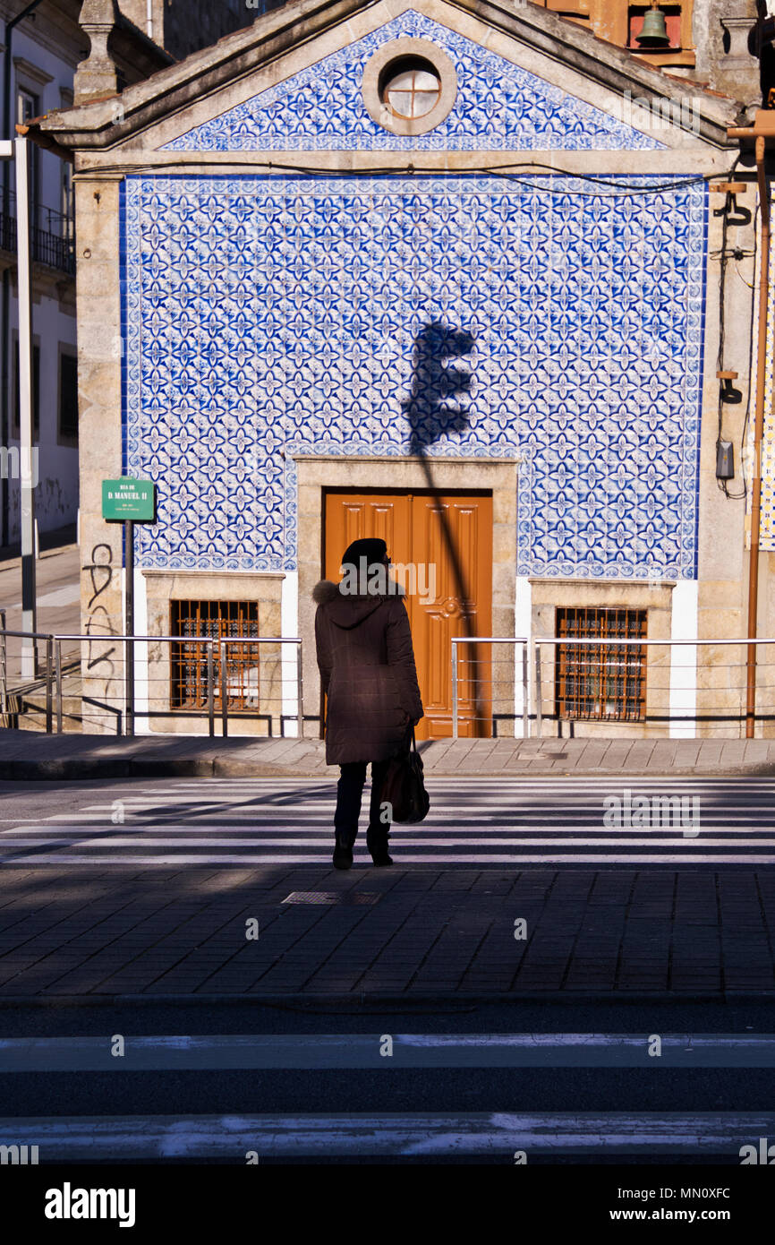 A woman waits to cross the road opposite a blue tiled building, Porto, Portugal Stock Photo