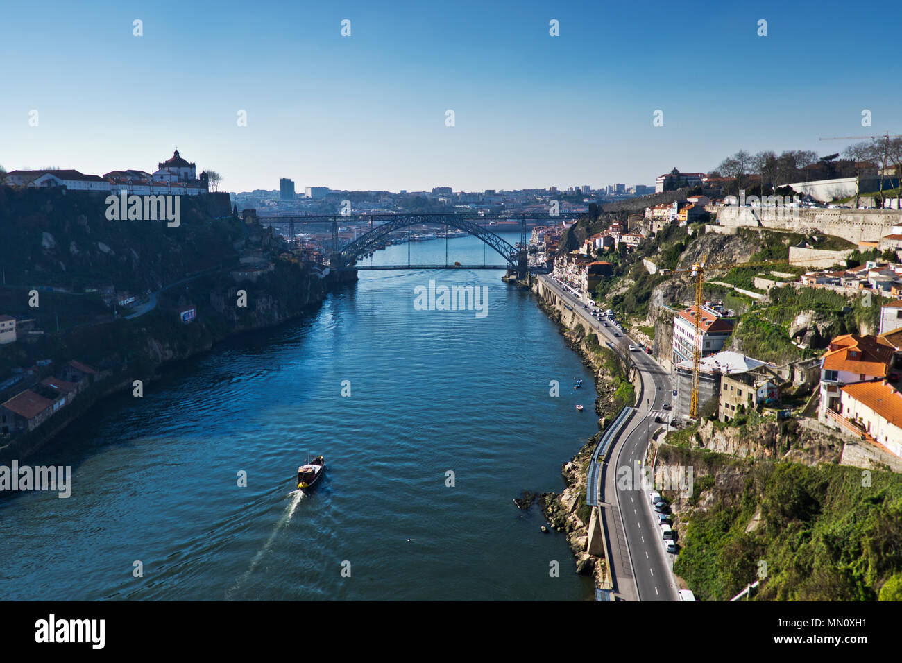 A boat heads along the River Douro in Porto towards the Dom Luis I bridge. Stock Photo