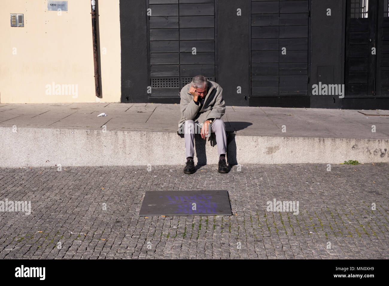 A man sits alone holding his head in a street in Porto, Portugal Stock Photo