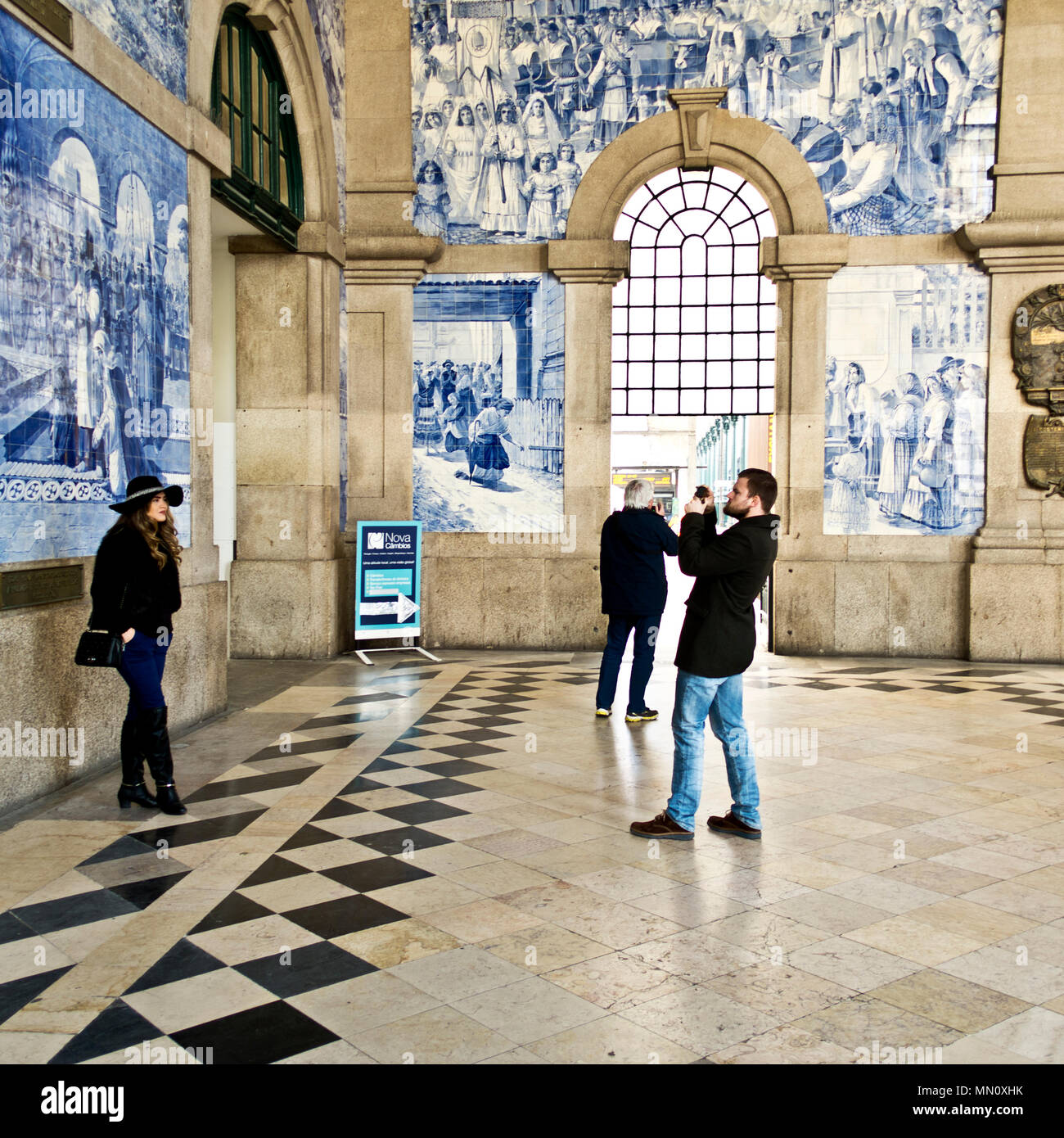A man takes a photo of a woman using a small camera inside the Sao Bento railway station, Porto, Portugal Stock Photo
