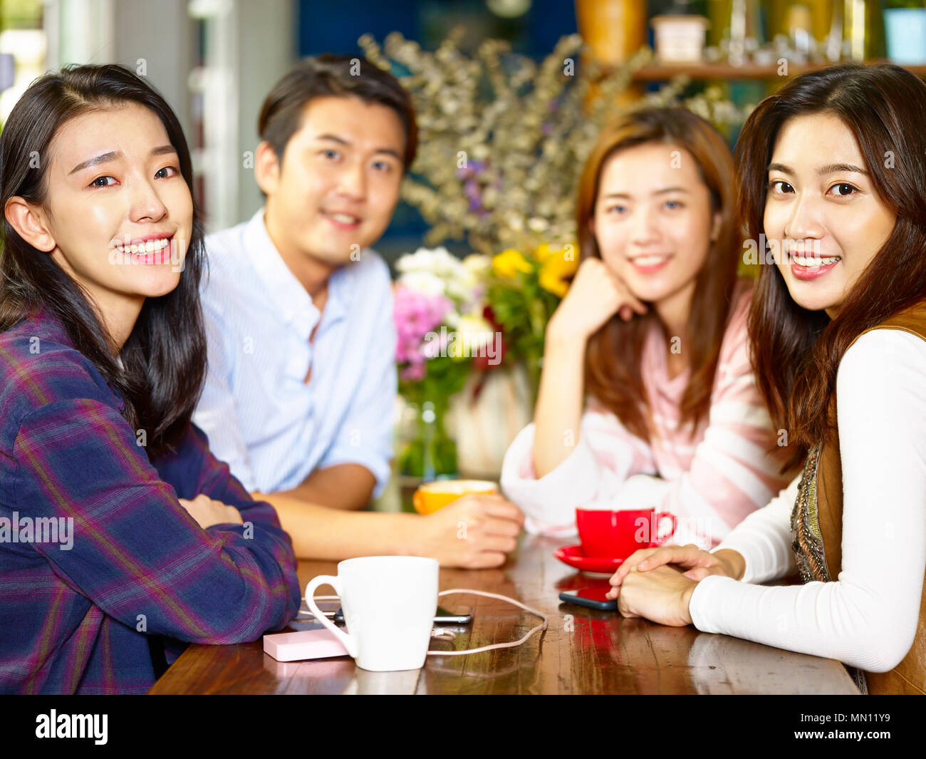 group of four happy asian young adults man and woman looking at camera smiling while gathering in coffee shop. Stock Photo