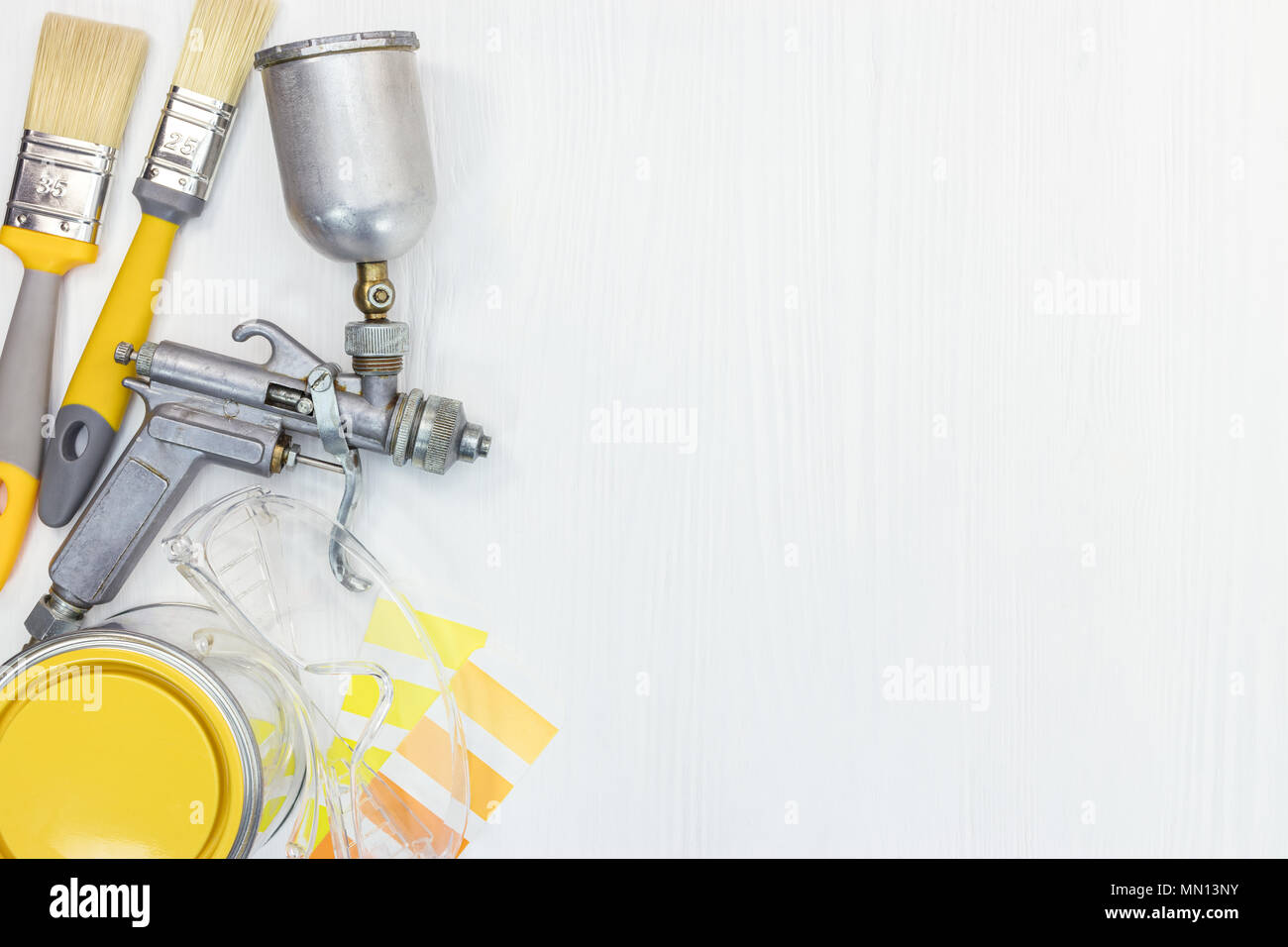 housework tools flat view. paintbrushes, can, protective glasses, color swatches and paint spray gun on white wooden background  Stock Photo