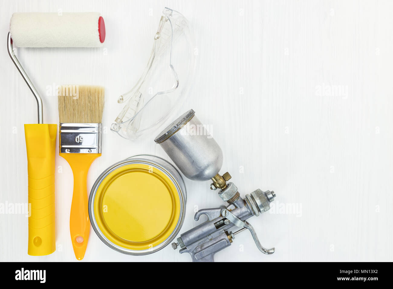paint roller, brush, safety glasses, compressor paint sprayer, yellow paint can on white wooden background, flat lay Stock Photo