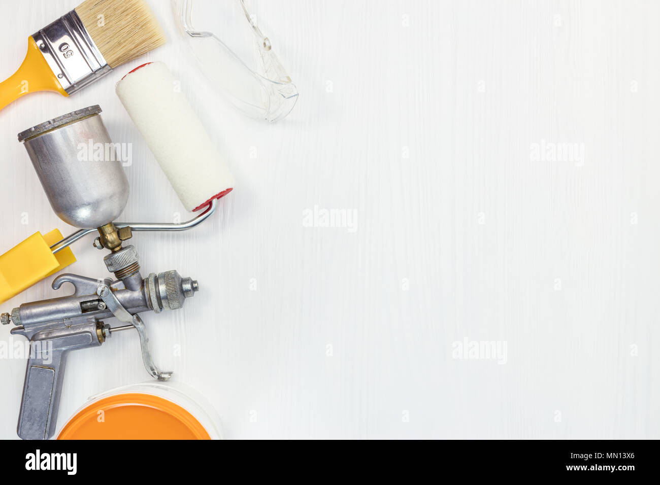paint roller, brush, protective  glasses, spray gun, can with orange paint on white wooden background. renovation tools flat view Stock Photo