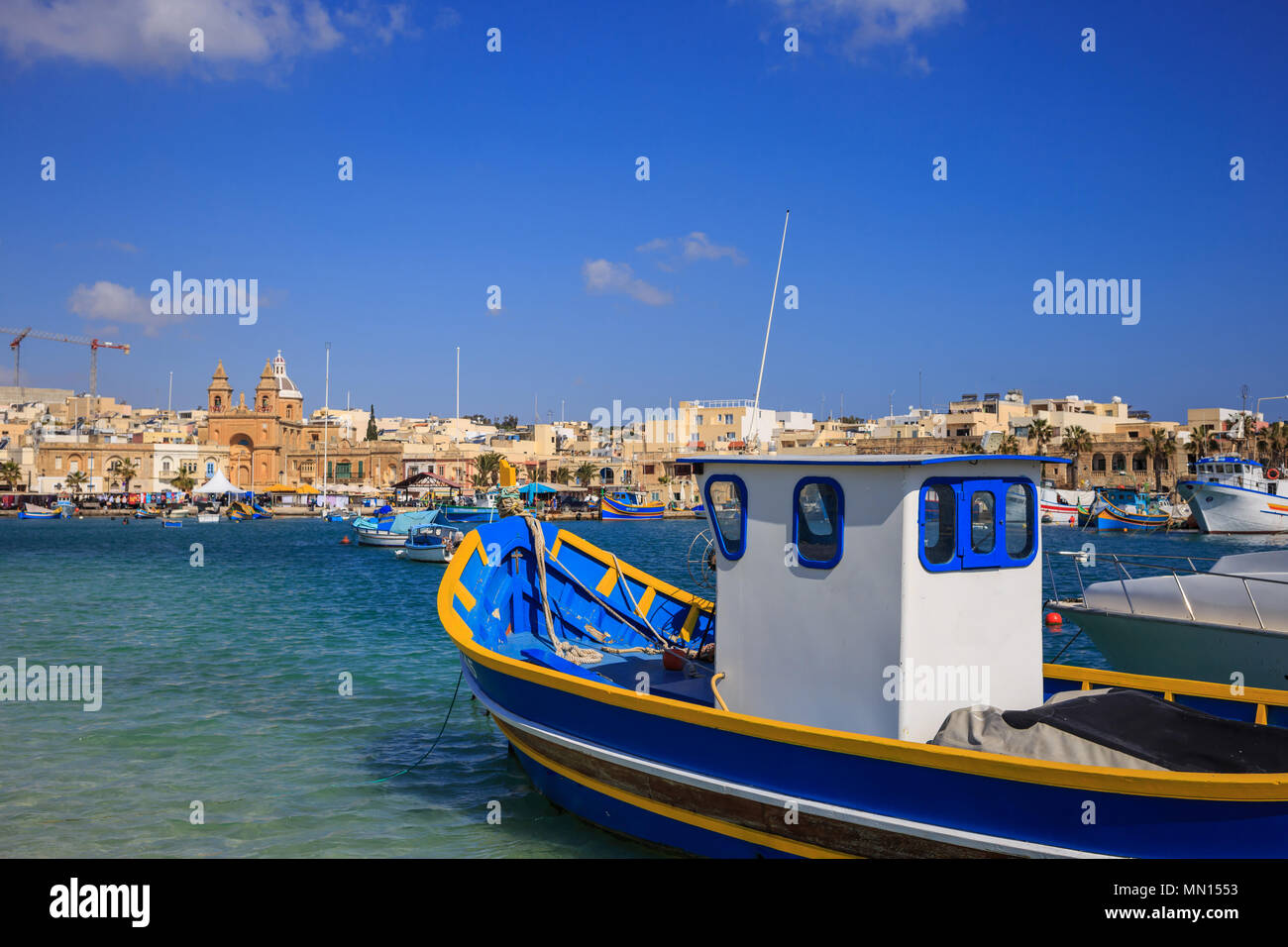 Traditional colorful fishing boats, luzzu, anchored at Marsaxlokk, the historic port of Malta. Blue sky and village background. Close up view. Stock Photo