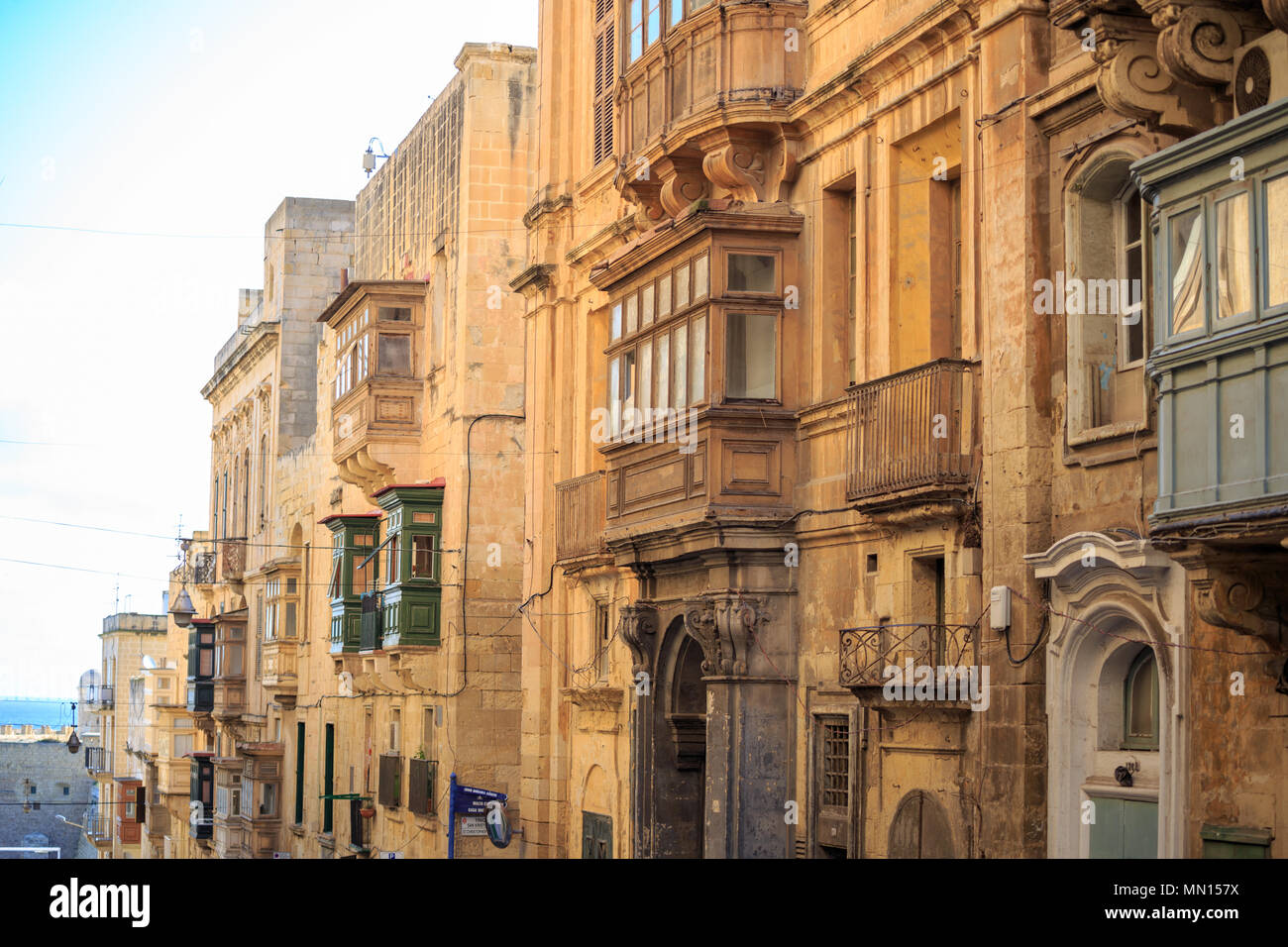 Malta, Valletta, traditional sandstone buildings with colorful wooden windows on covered balconies. Blue sky with clouds and sea background. Stock Photo