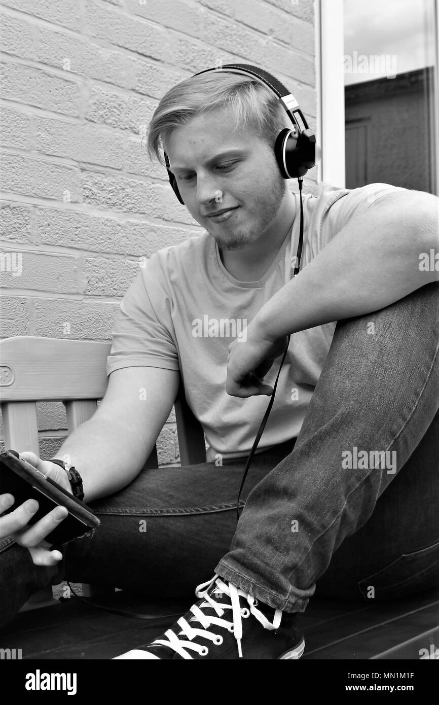 Seventeen year old teenage Caucasian male using headphones to listen to music through his smartphone. Stock Photo