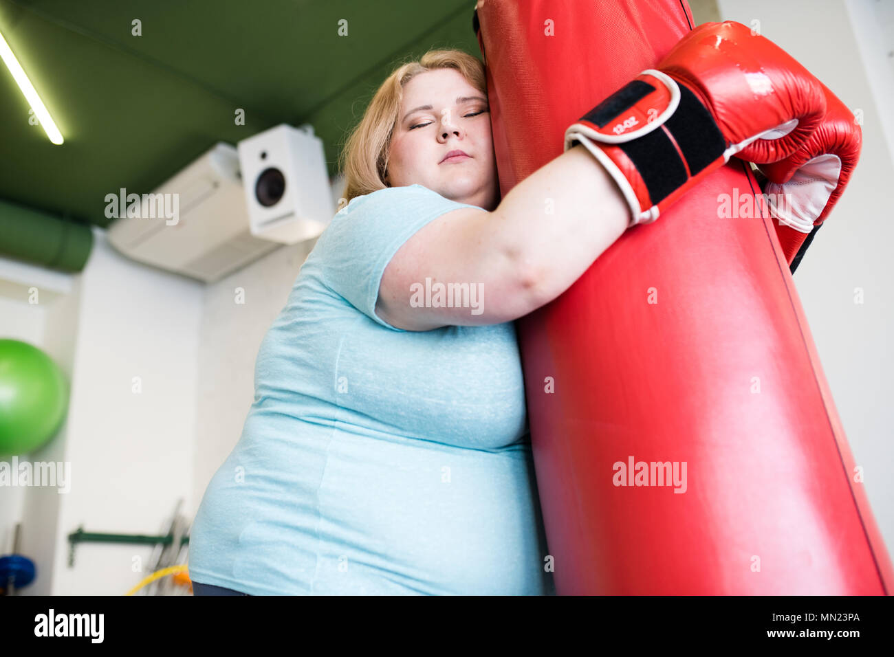 Low angle portrait of exhausted obese woman leaning on punching bag with eyes closed after extreme weight loss training in gym copy space Stock Photo Alamy