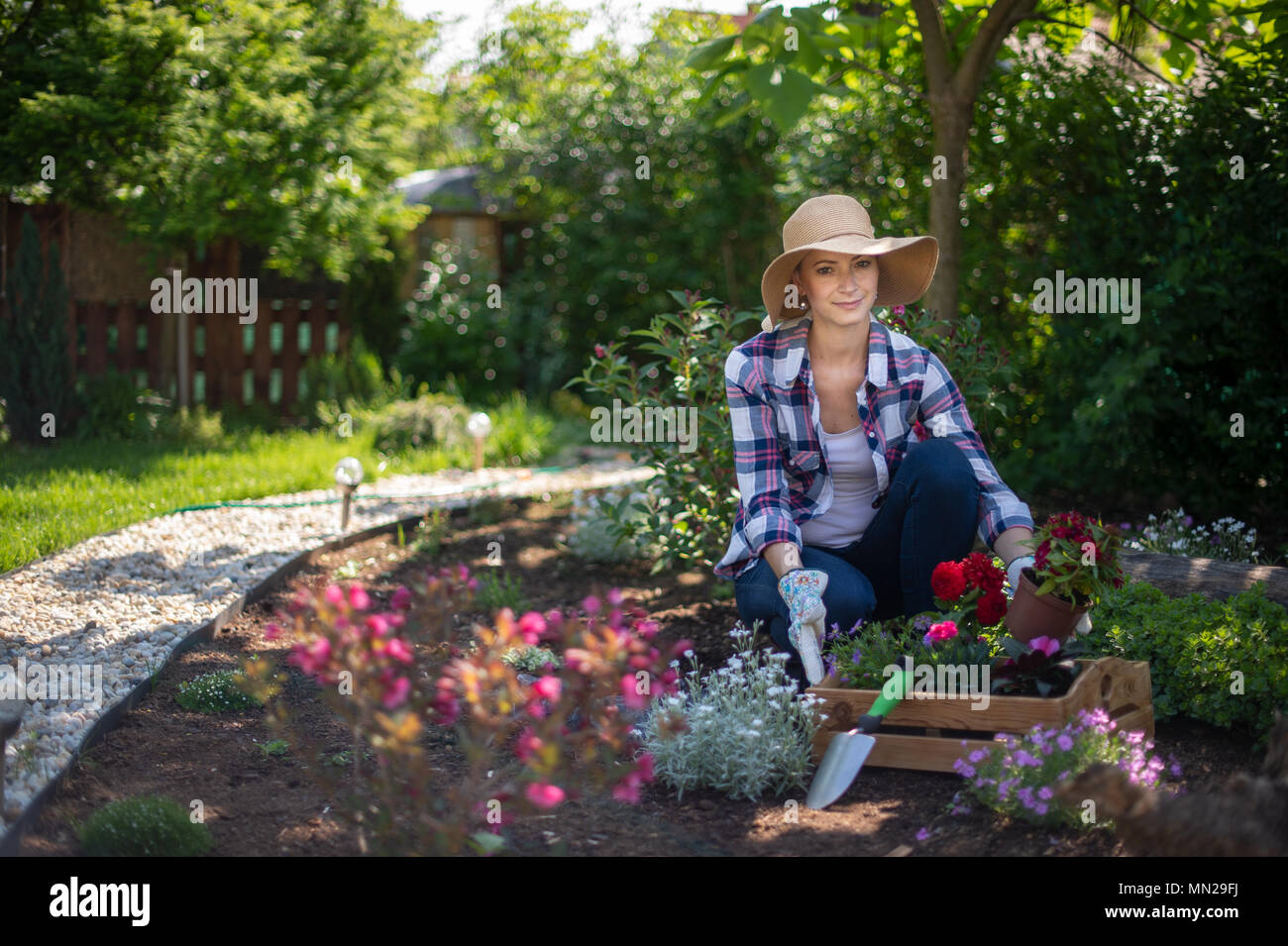 Beautiful female gardener looking at camera smiling and holding wooden crate full of flowers ready to be planted in her garden. Gardening concept. Stock Photo