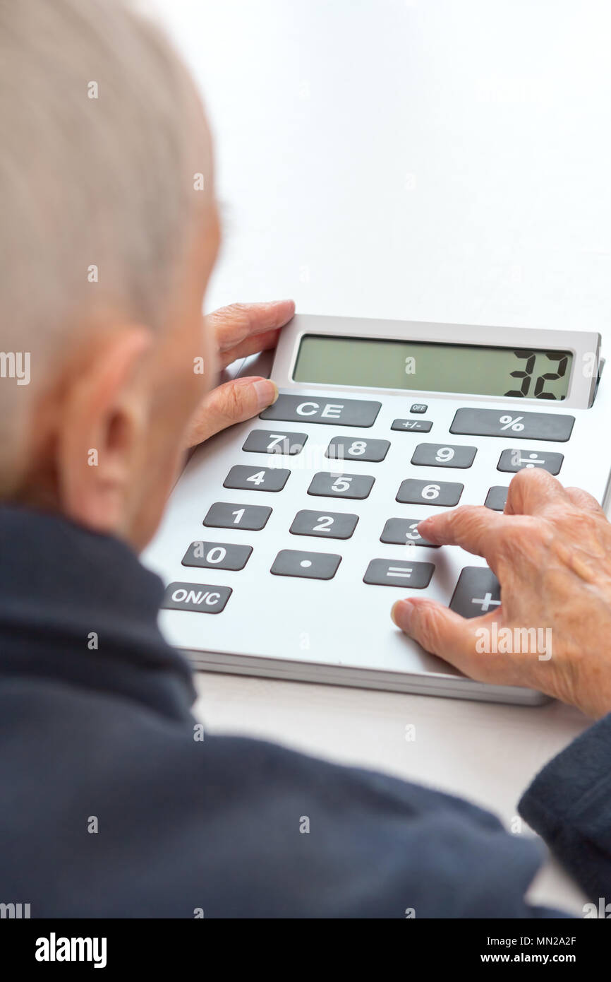 Very old and visually impaired woman sitting at a table using a desktop calculator with an extra large keypad Stock Photo