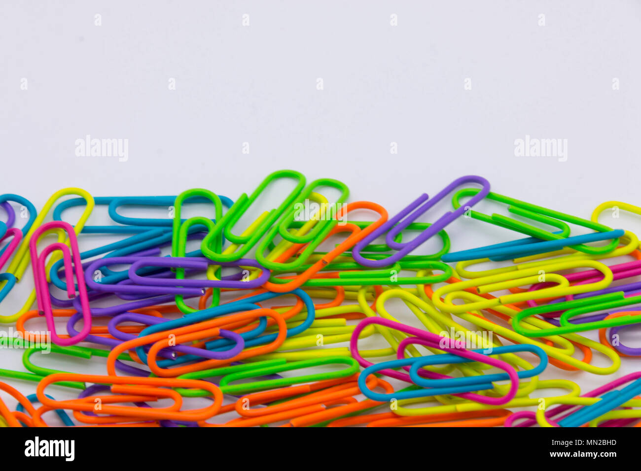 A pile of brightly coloured paper clips on a white background Stock