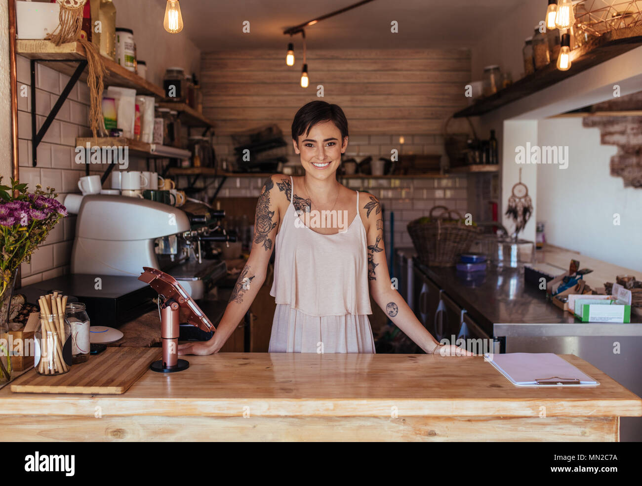 Woman standing at the billing counter of her cafe posing. Smiling restaurant owner standing beside the billing machine. Stock Photo
