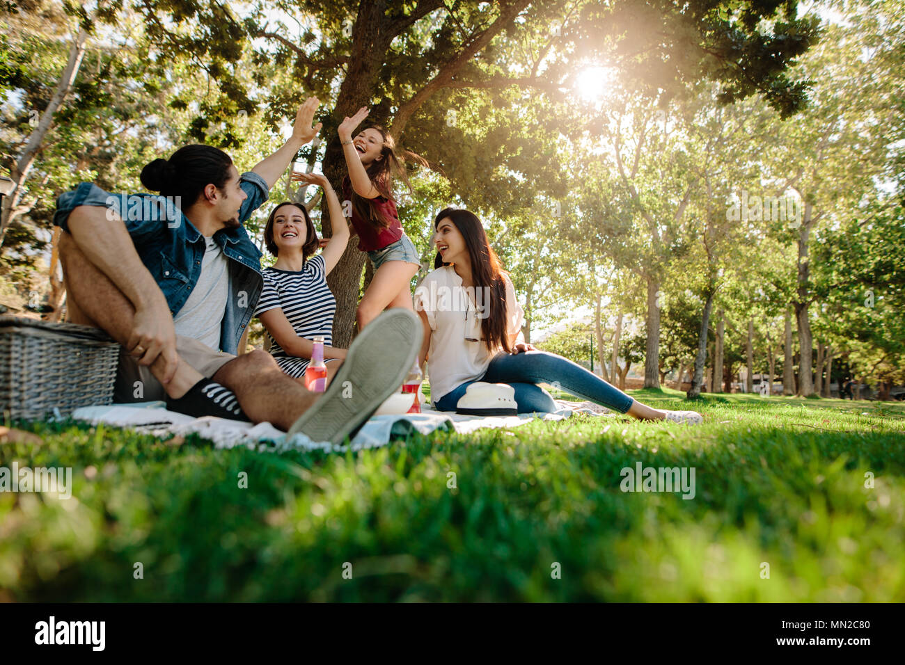 Woman giving high five to male friend at park. Group of young people having great time at picnic. Stock Photo
