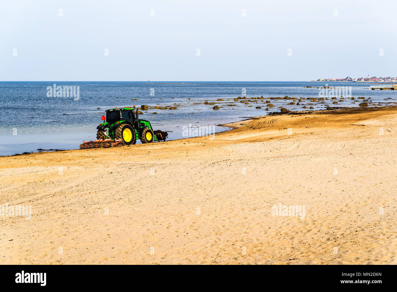 Domsten, Sweden - April 30, 2018: Documentary of everyday life and place. Green John Deere 6120 tractor cleaning up seaweed and stones from the beach  Stock Photo