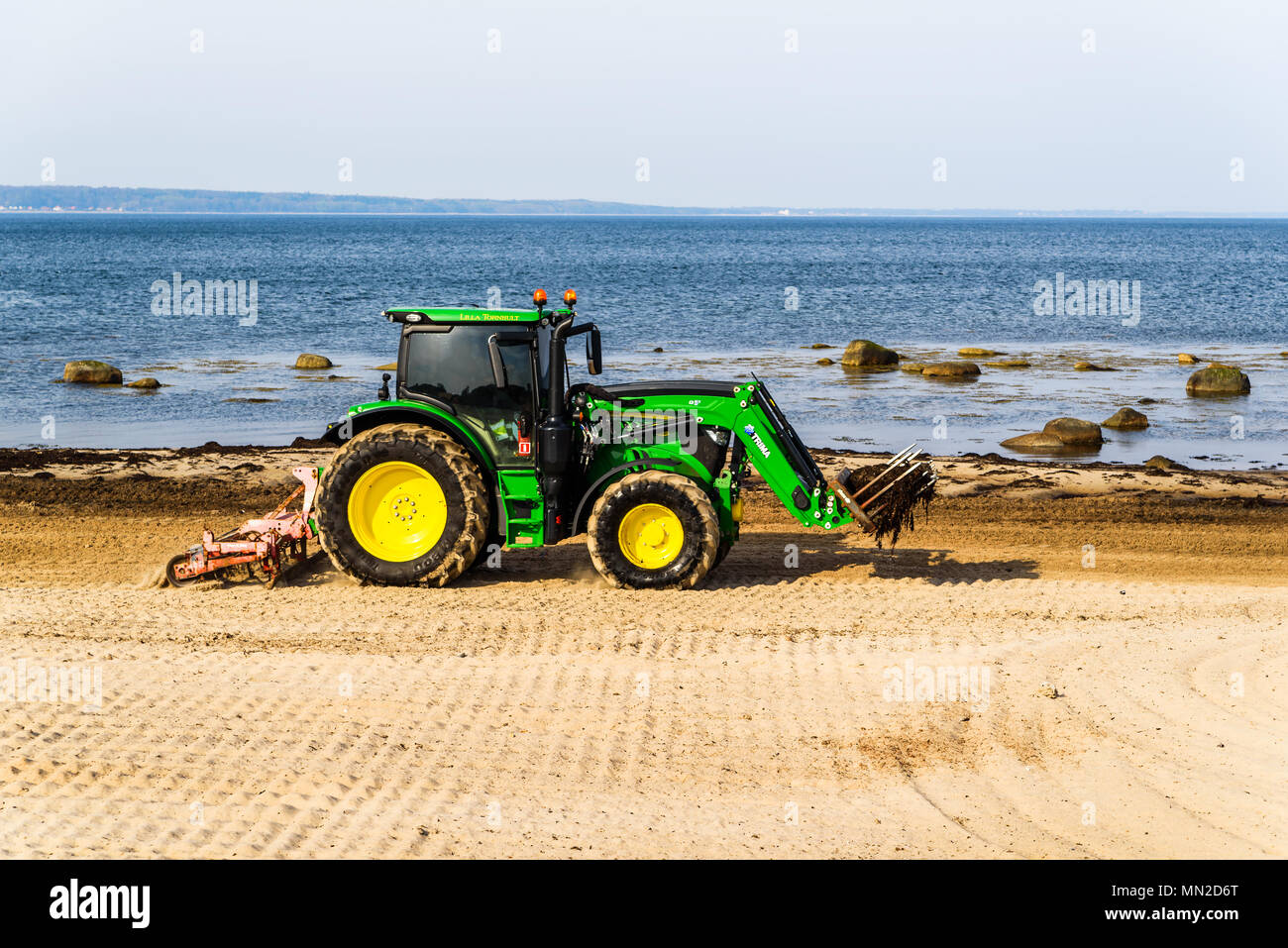 Domsten, Sweden - April 30, 2018: Documentary of everyday life and place. Green John Deere 6120 tractor cleaning up seaweed and stones from the beach  Stock Photo