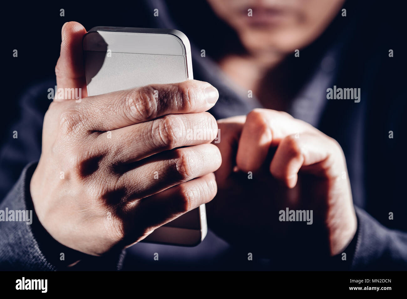 Hooded cyber crime hacker using mobile phone internet hacking in to cyberspace,online personal data security concept. Stock Photo