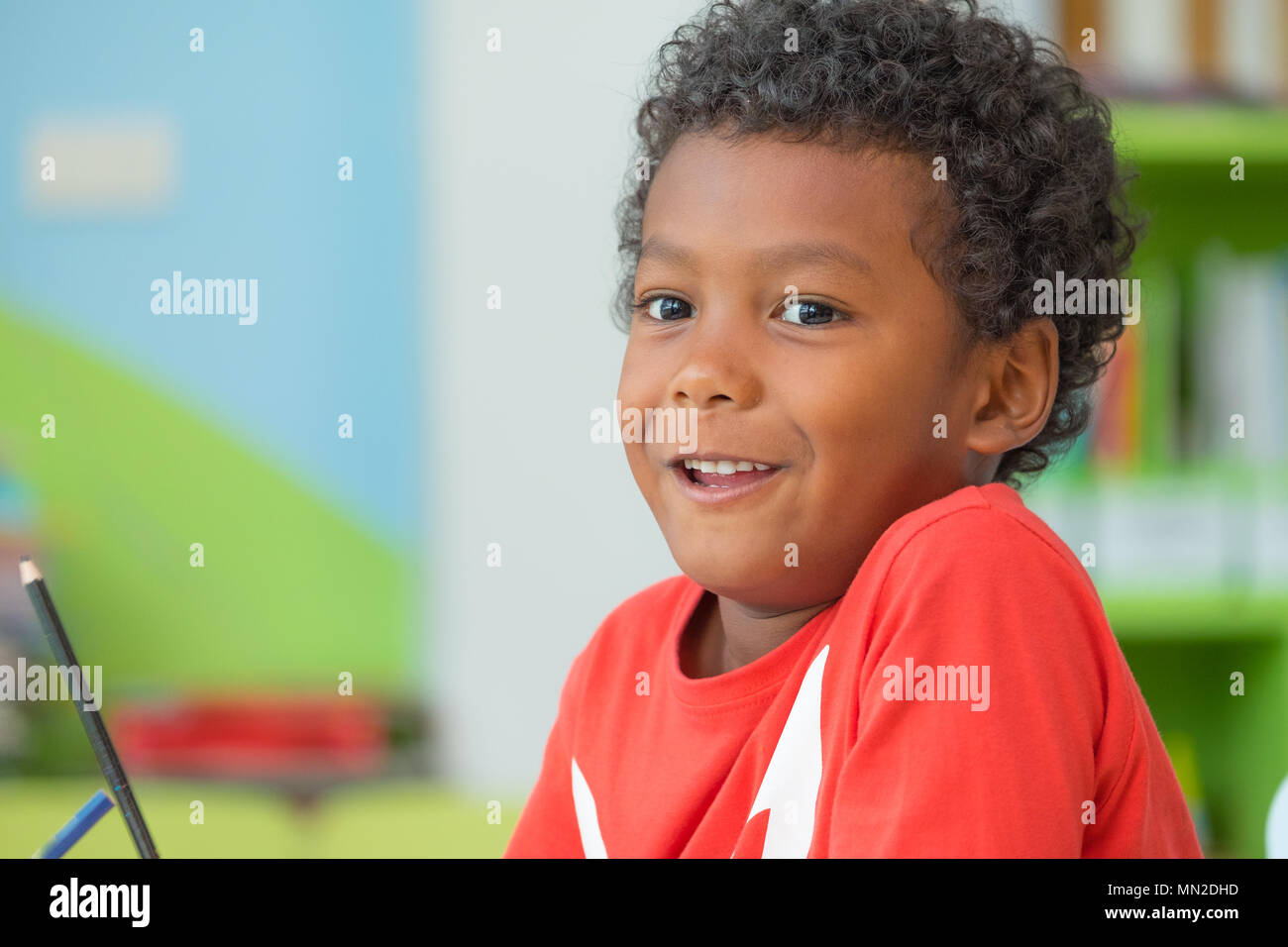 African American ethnicity kid holding group of color pencil smiling at library in kindergarten preschool classroom.education concept Stock Photo