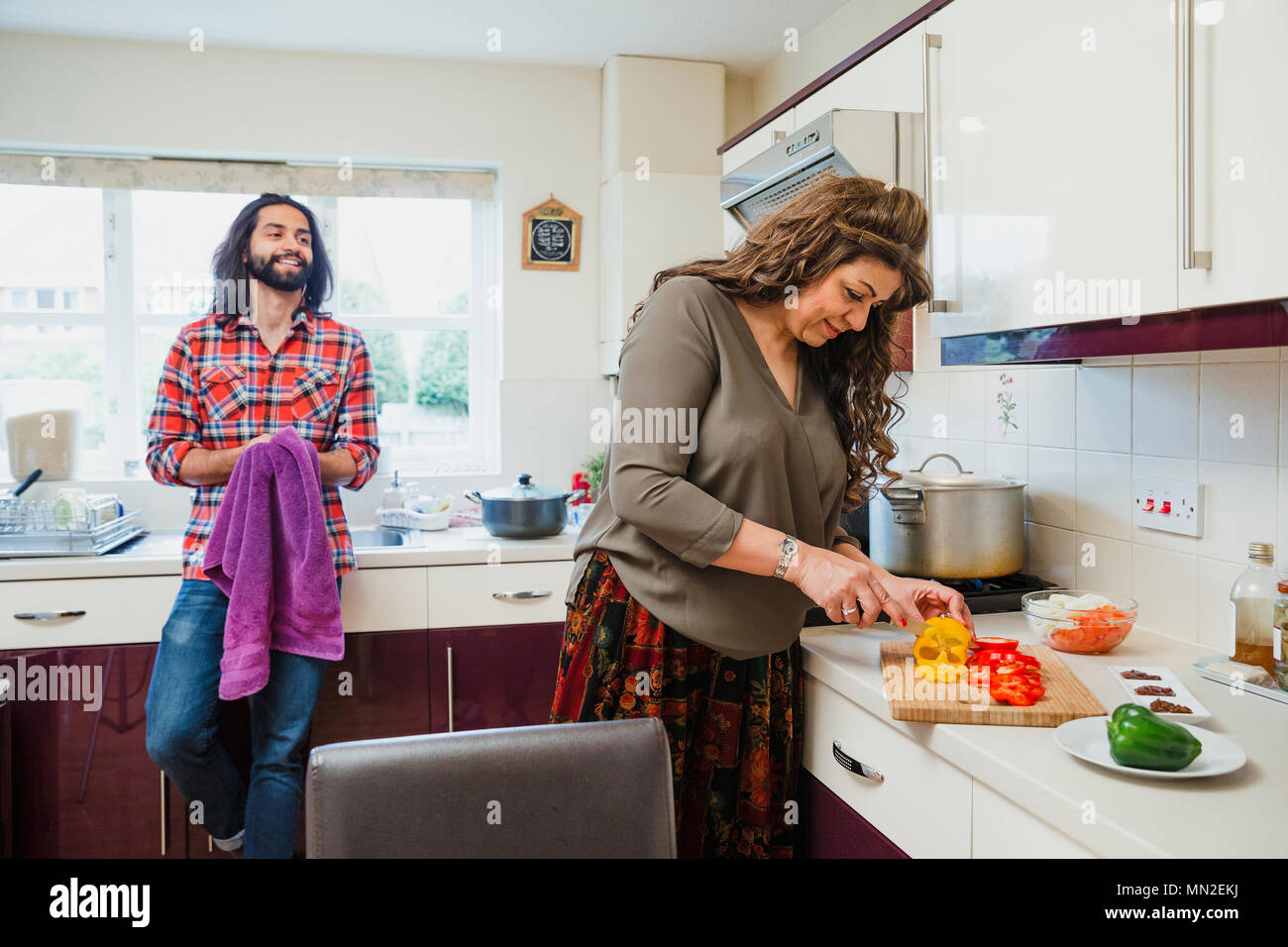 Mid adult man is relaxing in the kitchen talking to his mother while she prepares a curry on the cooker. Stock Photo