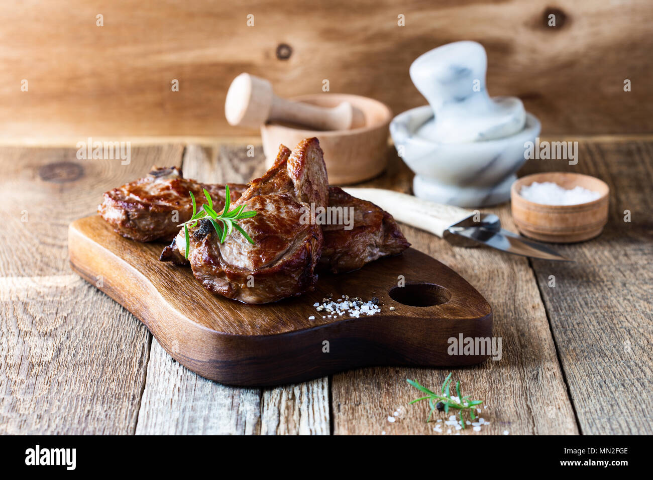 Roasted veal chops with herbs on rustic wooden cutting board, pan seared steak dinner Stock Photo