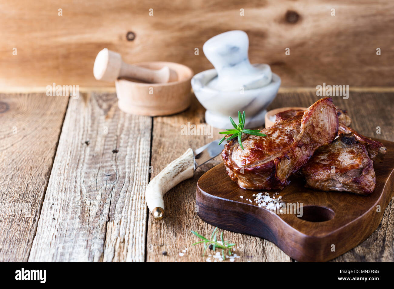 Roasted veal chops with fresh herbs on rustic wooden cutting board, pan