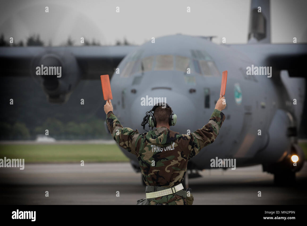 Senior Airman Kyle Knudsen, 374th Aircraft Maintenance Squadron crew chief, marshals a C-130J Super Hercules during Exercise Beverly Morning at Yokota Air Base, Japan, Aug. 18, 2017. The training is designed to test the ability of Airmen to survive in austere environments with chemical, biological, radiological, nuclear and explosive hazards. (U.S. Air Force photo by Yasuo Osakabe) Stock Photo