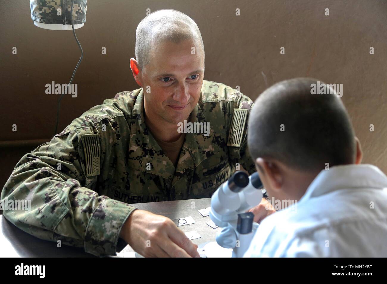 170823-A-QE286-0060 AGUAN, Honduras (August 23, 2017) U.S. Navy Lt. Cmdr. Ian Sutherland, technical director for the Navy Entomology Center of Excellence, helps a boy examine an insect through a microscope at Escuela Lidia Handal, during a Southern Partnership Station 17 community relations project (COMREL). SPS 17 is a U.S. Navy deployment executed by U.S. Naval Forces Southern Command/U.S. 4th Fleet, focused on subject matter expert exchanges with partner nation militaries and security forces in Central and South America. (U.S. Army photo by SPC Judge Jones/Released) Stock Photo