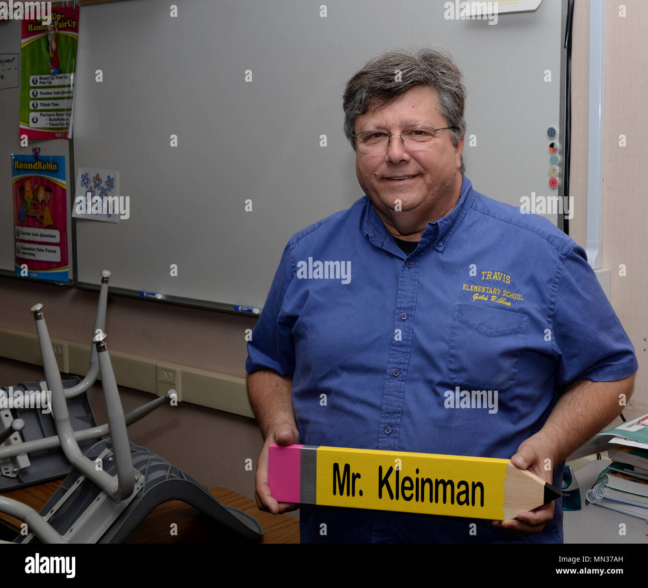 Mark Kleinman, a retired U.S. Air Force lieutenant colonel and a teacher at Travis Elementary School, poses for a photo while holding a pencil with his name on it that was given to him by one of his students at Travis Air Force Base, Calif., Aug. 25. Kleinman taught Airmen how to fly a variety of aircraft during his 33-year Air Force career and now teaches math, English language arts, science and history to 4th grade students. (U.S. Air Force photo by Tech. Sgt. James Hodgman) Stock Photo