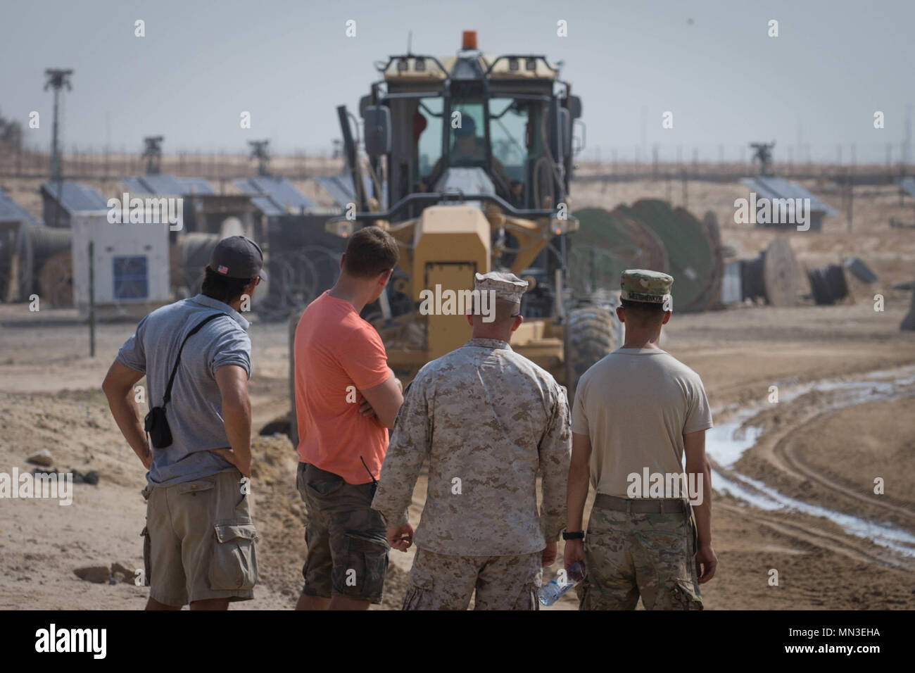 U.S. Service members observe a road grater as it digs trenches into the soil in order to make it malleable while deployed in the Middle East, Aug. 23, 2017. Special Purpose Marine Air-Ground Task Force – Crisis Response – Central Command Marines with Marine Wing Support Squadron 372 practiced interoperability with other military branches while testing the durability and life expectancy of a new road-building product. Stock Photo