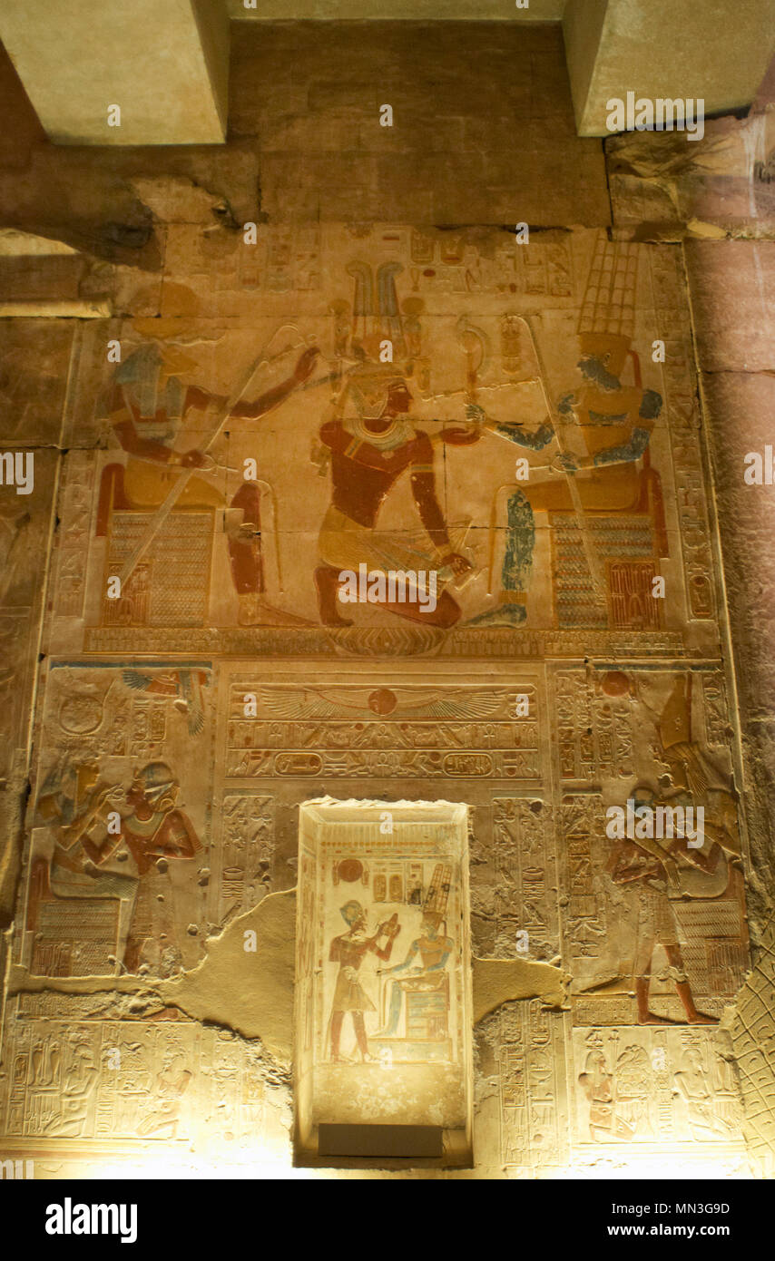 Egypt. Abydos. Temple of Seti I. New Kingdom. 19th Dynasty. Relief with original polychrome, The Second Hypostyle Hall. The Pharaoh Seti I kneeling while he receives emblems from god Amun (wearing two vertical plumes on his head). God Khnum to the left (head of a ram). 1292-1189 BC Stock Photo