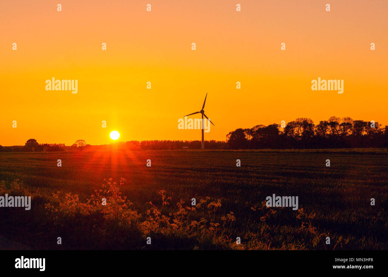 Glowing orange and red sunset over a Yorkshire Village with wind turbine to the right.  Sunset to the left.  England, UK, Landscape Stock Photo