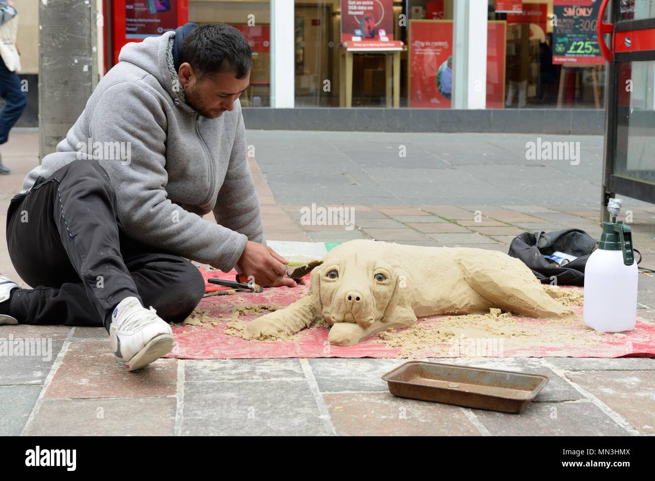 An eastern european man carves a dog from sand on Buchanan Street, Glasgow, Scotland, UK. Stock Photo